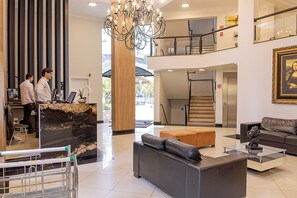 A hotel lobby with a reception desk, a chandelier, a staircase, and a seating area. - Havana Palace Hotel I (Uberaba)