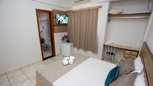 Une chambre d’hôtel avec un lit, un bureau, une chaise, une télévision et une salle de bain visible à travers une porte ouverte.