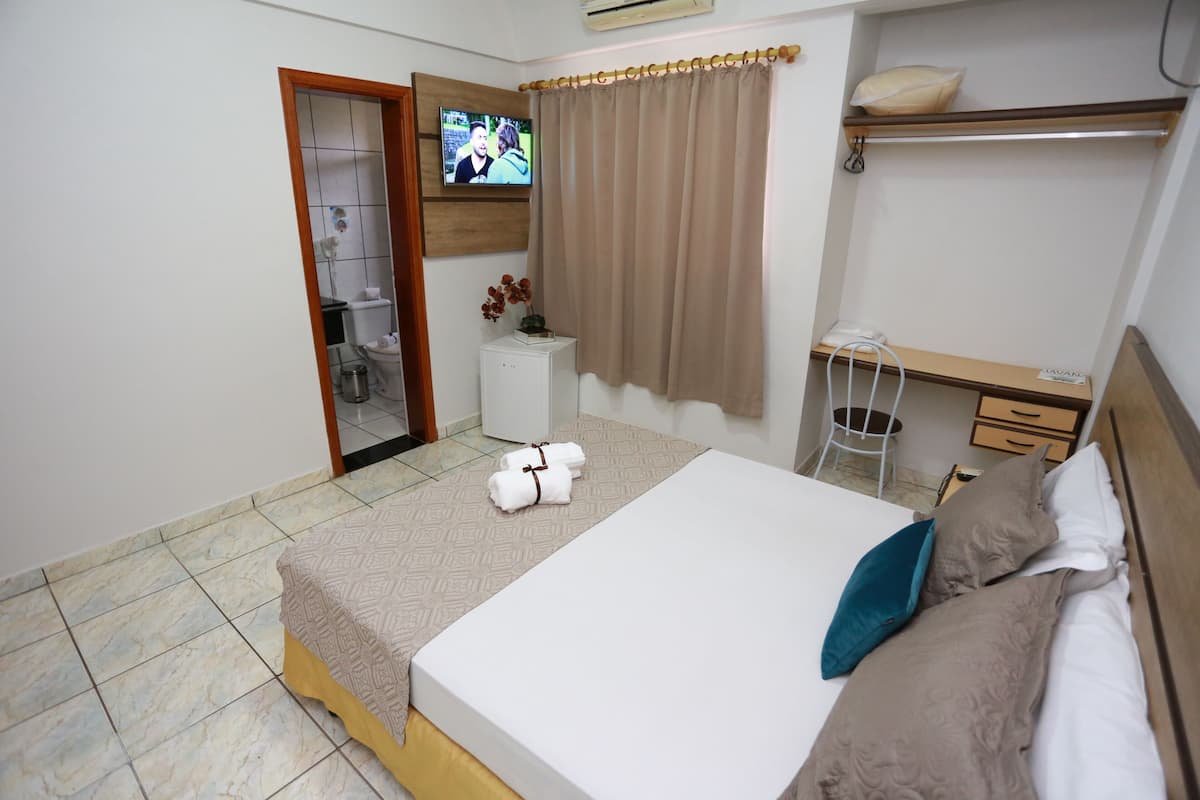 Habitación de hotel con cama, escritorio, silla, televisión y baño visible a través de una puerta abierta.
