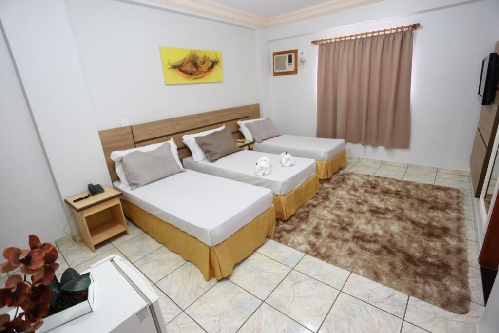 A room with two single beds, a small bedside table with a lamp, a large fluffy rug, and a painting on the wall.