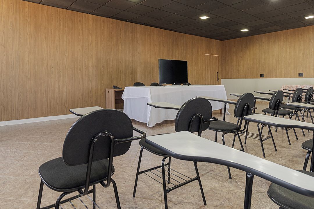Un salón de conferencias con filas de mesas y sillas, un televisor de pantalla plana grande y una pared de madera.