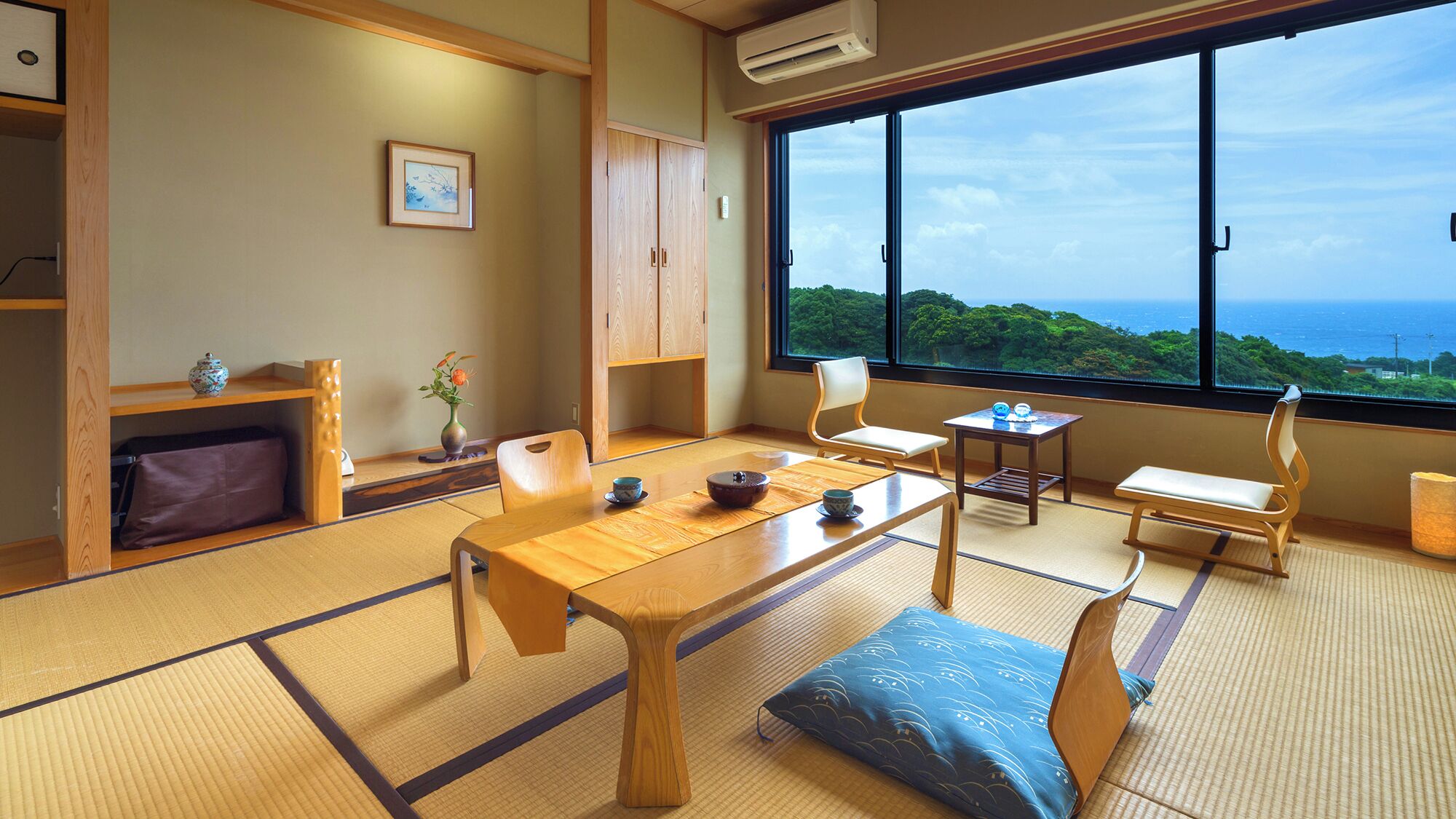 Una habitación japonesa tradicional con suelo de tatami, una mesa baja, cojines y vistas al mar.