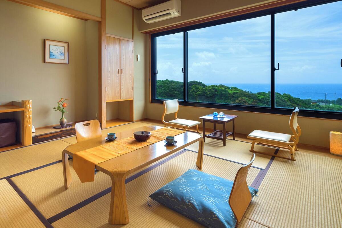 A traditional Japanese room with tatami flooring, a low table, cushions, and a view of the sea.