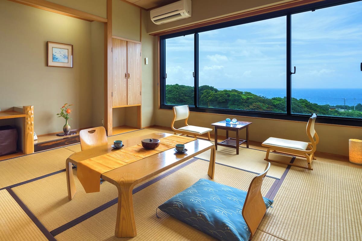 Una habitación japonesa tradicional con suelo de tatami, una mesa baja, cojines y vistas al mar.