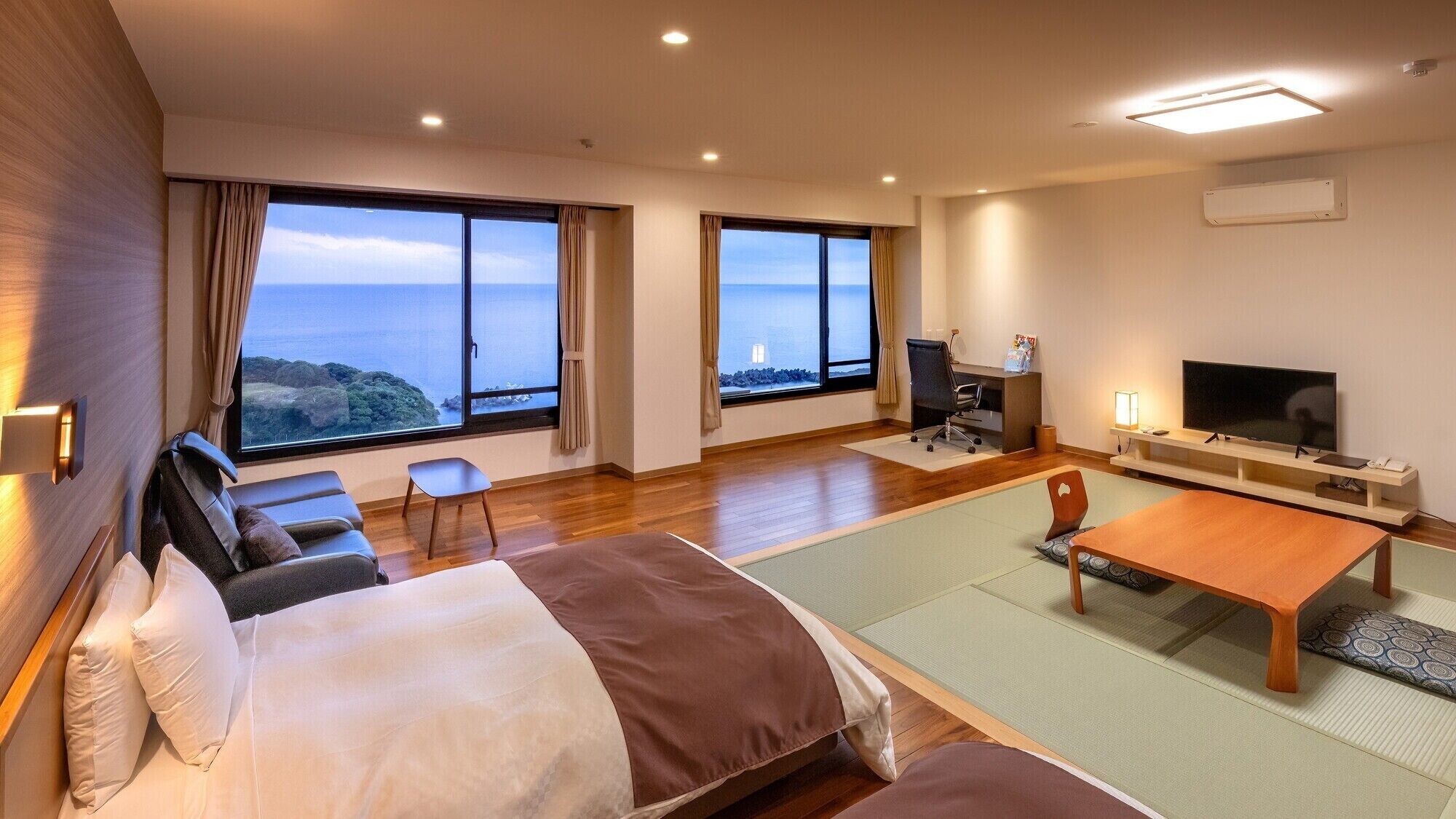 Habitación de hotel con cama, escritorio, televisión y ventanas amplias con vistas.
