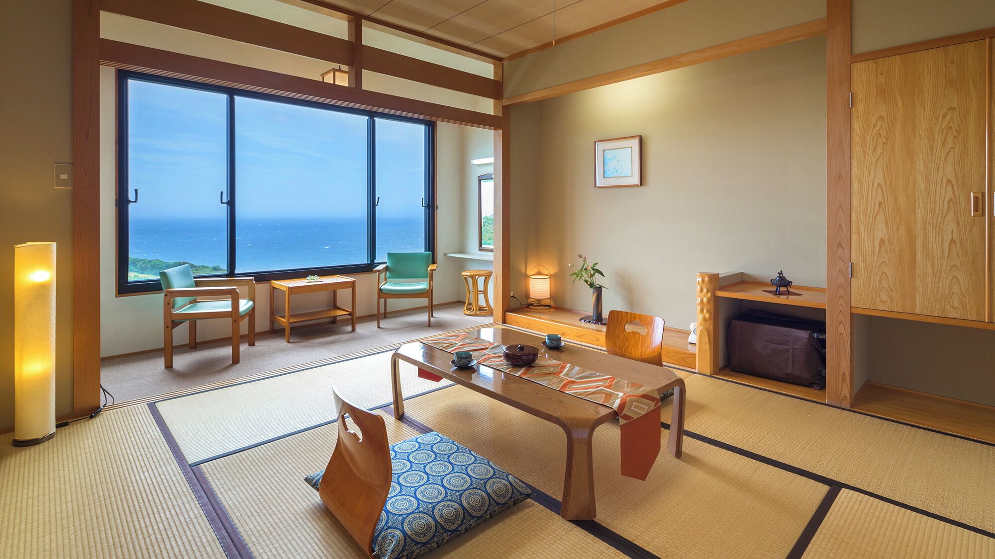 Una habitación japonesa tradicional con suelo de tatami, una mesa baja, sillas, vista al mar y un armario de madera.
