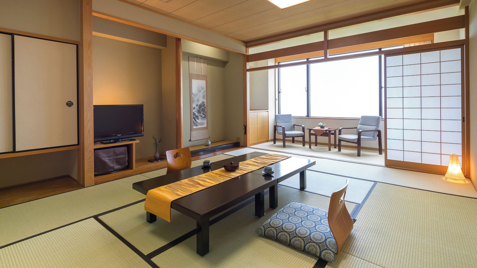 Una habitación japonesa tradicional con suelo de tatami, una mesa baja, televisor, puertas correderas y vistas a través de un gran ventanal.