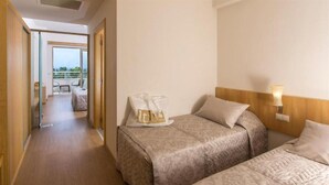 Habitación de hotel con dos camas, un balcón con vistas y un pequeño rincón de descanso.