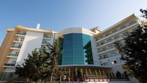 Un hotel de varios pisos con fachada central de vidrio, balcones en cada planta y techo plano.