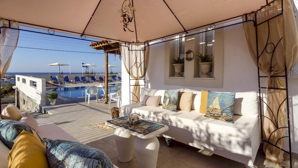 A covered outdoor seating area with a pool view, white furniture, and potted plants.