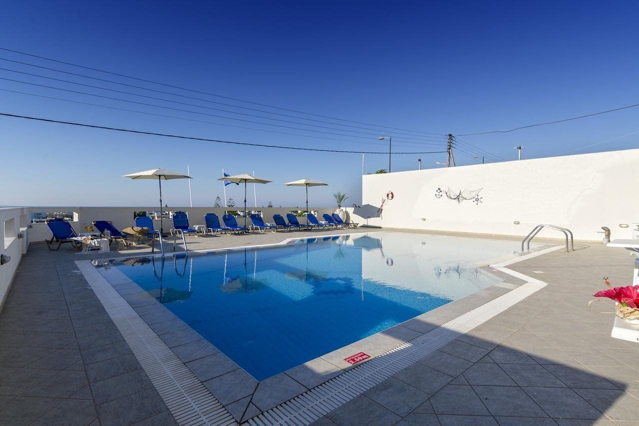 A swimming pool with blue water, surrounded by blue lounge chairs and umbrellas.