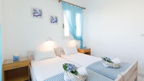 A hotel room with two beds, a nightstand, a lamp, and a window with a blue curtain.