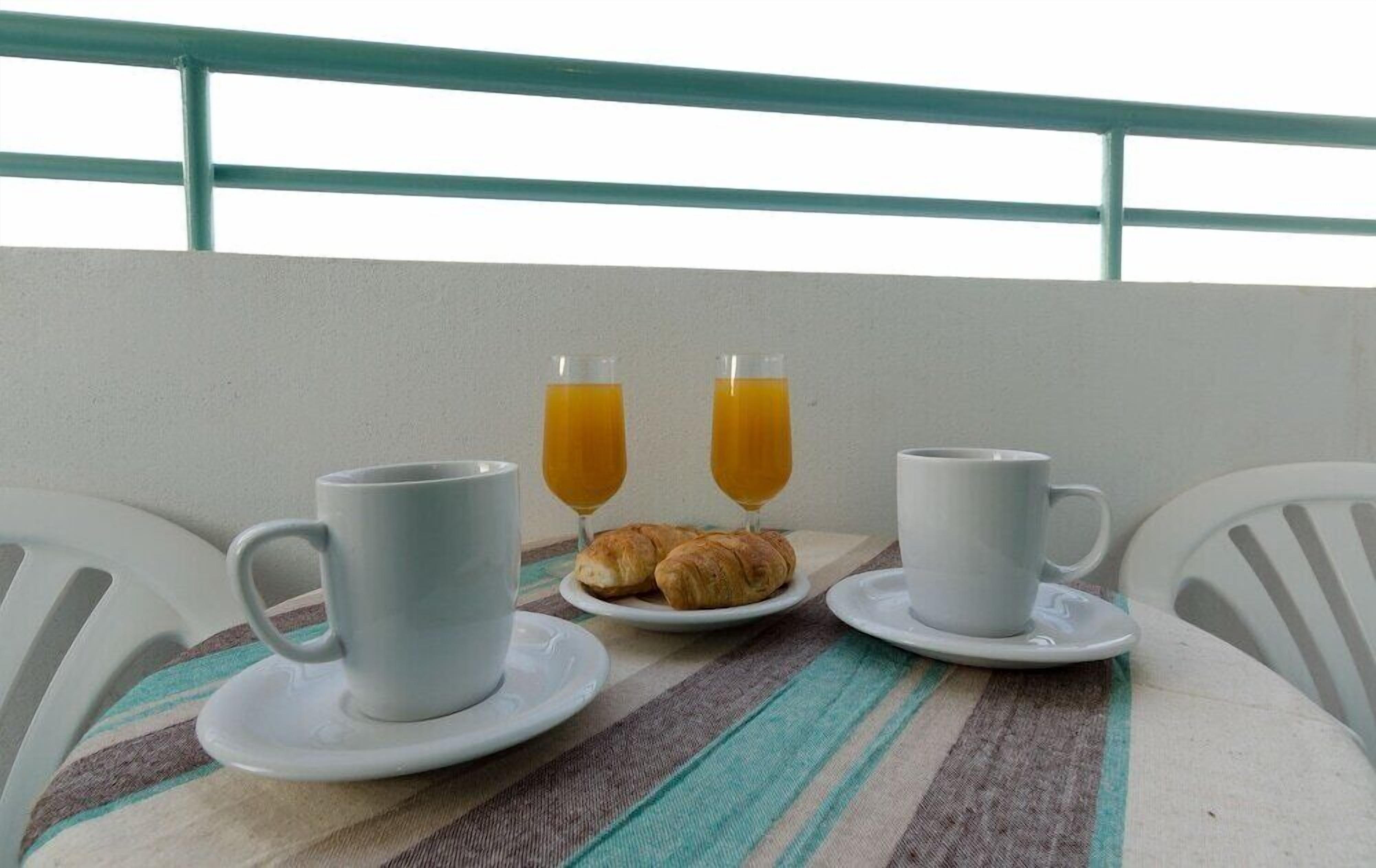 A table with two white cups and saucers, two glasses of orange juice, and a plate with croissants.