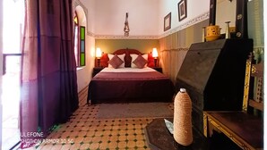 A hotel room with a bed, a nightstand, a lamp, a mirror, and a decorative vase. - Riad Zagouda (Marrakech)