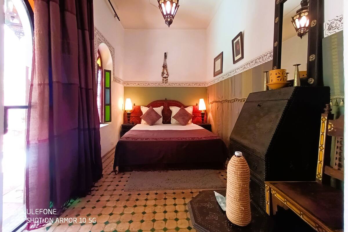 A hotel room with a bed, a nightstand, a lamp, a mirror, and a decorative vase.