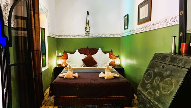 A room with a bed, two nightstands, a hanging lamp, and a decorative chest. - Riad Zagouda (Marrakech)