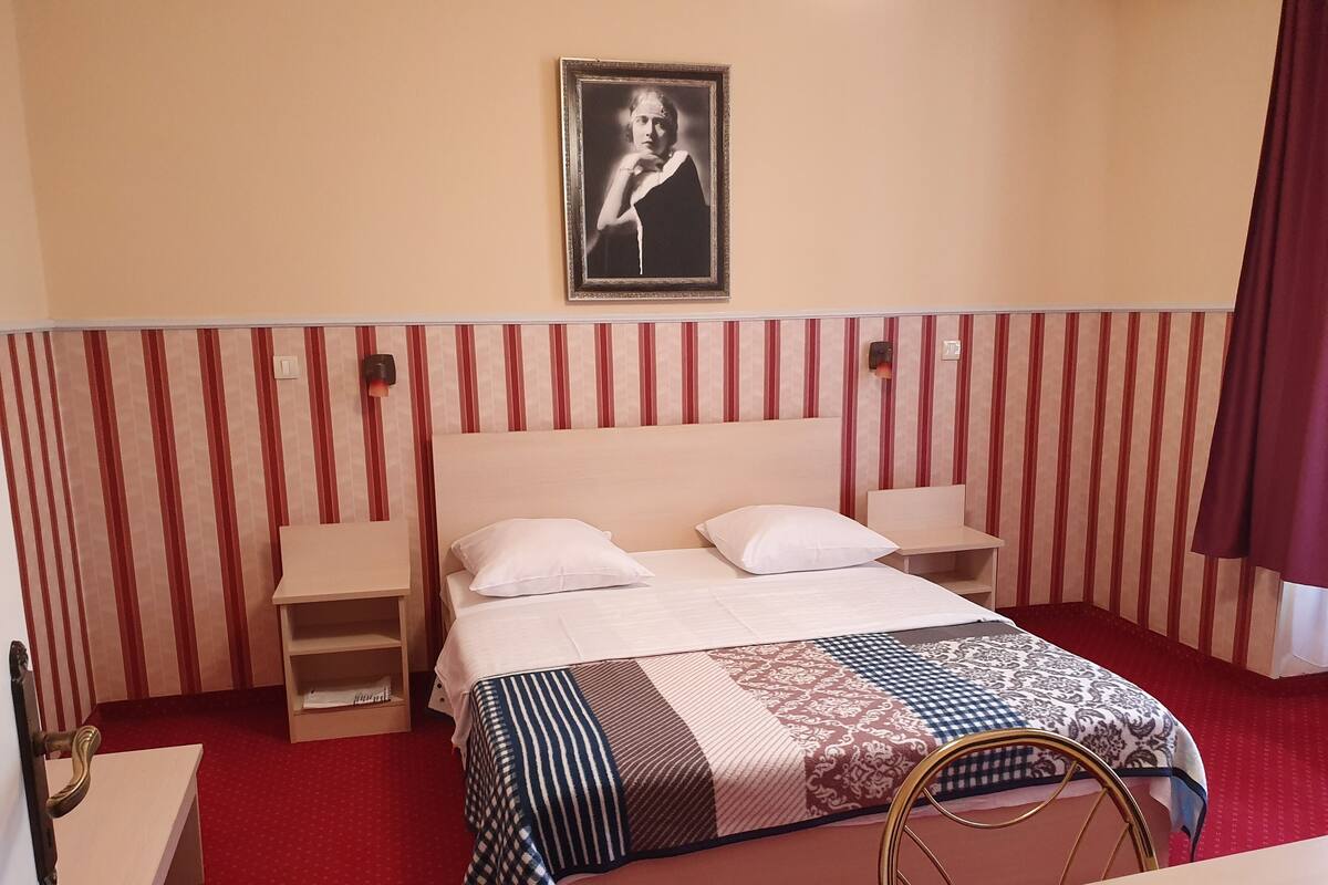 A hotel room with a bed, bedside tables, a chair, a framed portrait on the wall, and a striped wall design.