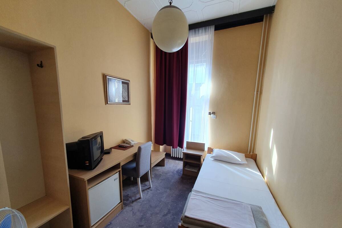 A hotel room with a bed, desk, chair, television, and a small cabinet.