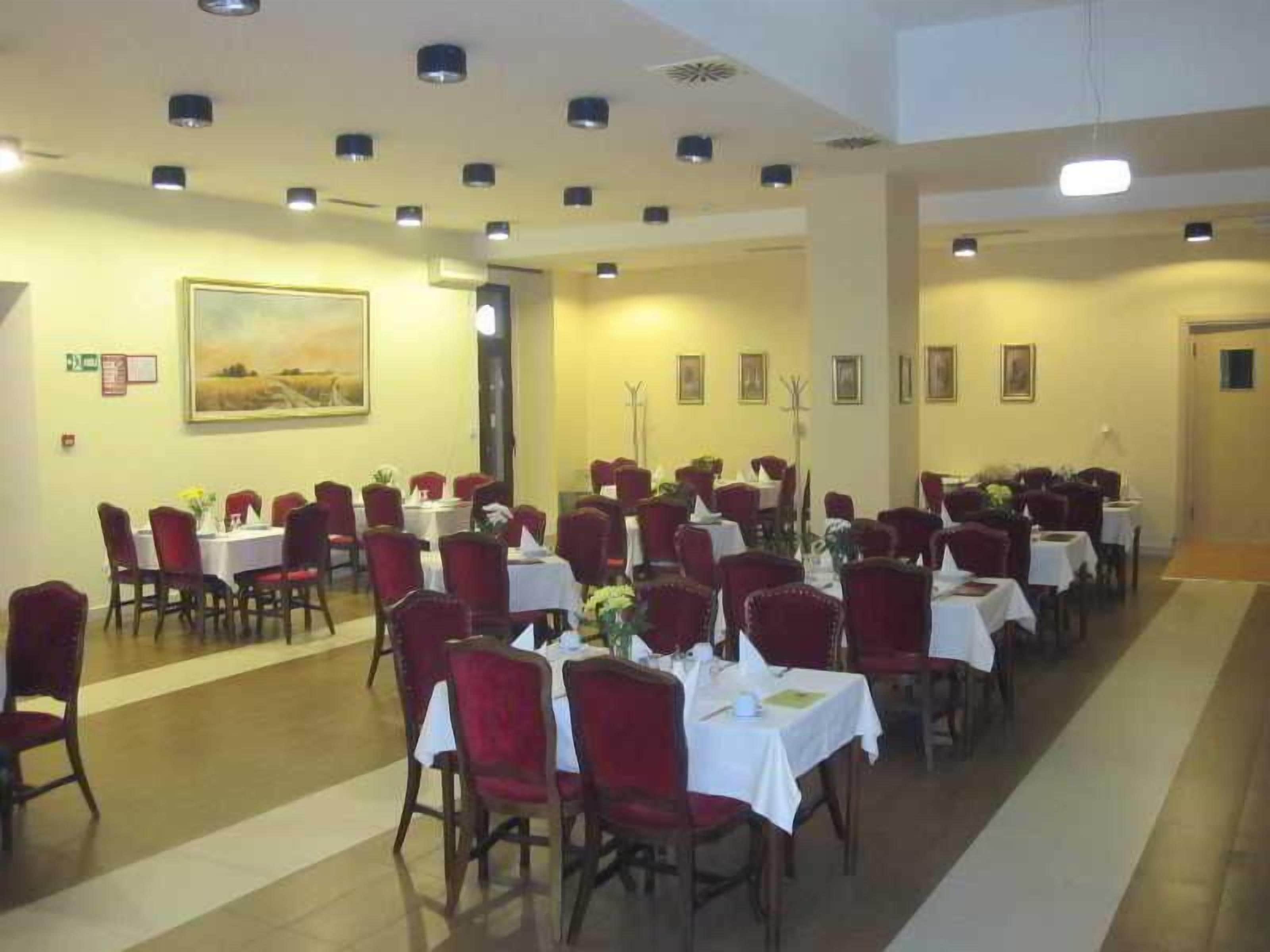 A dining area with tables and chairs, a painting on the wall, and a corridor leading to another room.