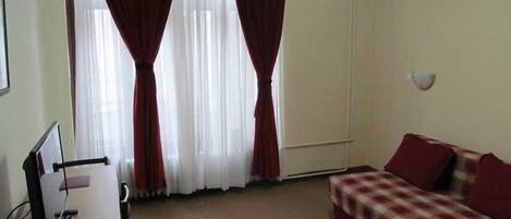 A room with a bed, a desk, and a window with curtains.