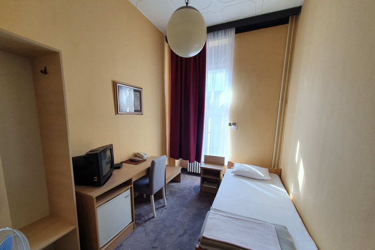 Habitació d'hotel amb llit, escriptori, cadira, televisió i un petit armari.