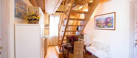 Un pasillo estrecho con vigas de madera, un banco blanco, una mesa con flores y un cuadro en la pared.