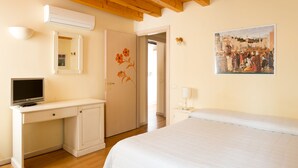 A bedroom with a bed, a desk with a TV, a painting on the wall, and a door with a floral design. - Ca' Dei Fuseri (Venice)