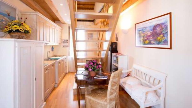 A narrow hallway with a wooden staircase, white cabinets, a dining table with flowers, and a white bench. - Ca' Dei Fuseri (Venice)