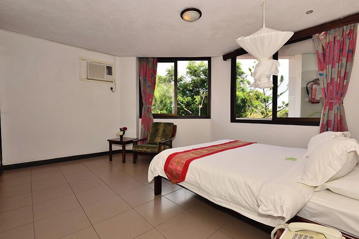 Una habitación de hotel con una cama grande, una silla, una mesita y una ventana con cortinas.