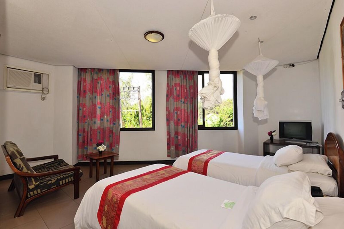 Habitación de hotel con dos camas, televisión, una silla y una mesa.