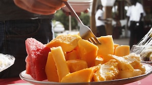 Un plato de fruta con un tenedor, un bol y una persona al fondo.