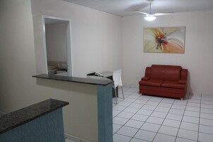 Quarto com sofá de couro vermelho, uma mesa branca e um quadro na parede.