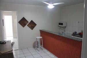 Cozinha com bancada branca, micro-ondas e duas pinturas penduradas na parede.