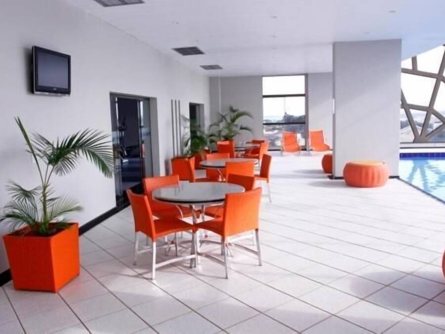 Un espace piscine intérieur moderne, avec des chaises et des tables orange, une grande fenêtre et un téléviseur à écran plat fixé au mur.
