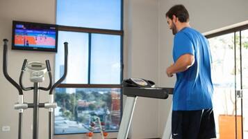 A man exercising on a treadmill in a room with a large window, a TV, and exercise equipment.