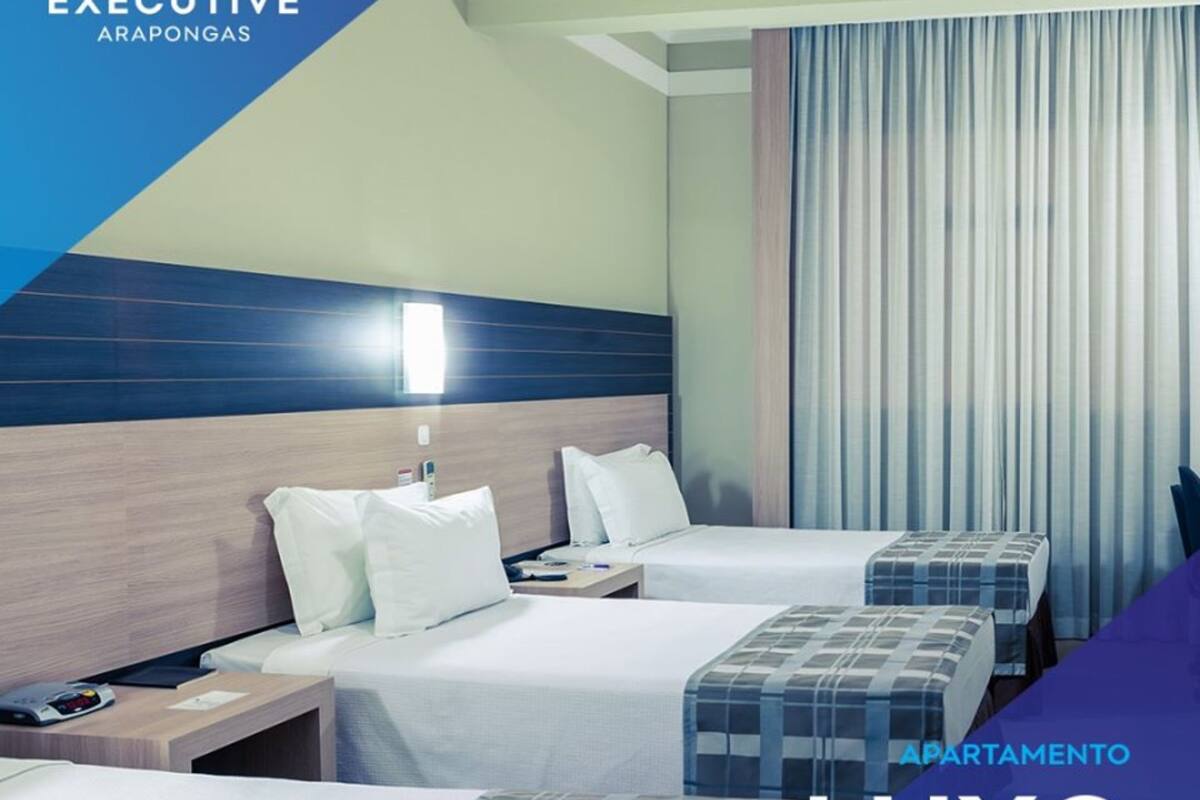 Habitación de hotel con dos camas, una mesita de noche y una ventana con cortinas. La habitación tiene un diseño moderno con una pared azul de acento y un cabecero de madera.