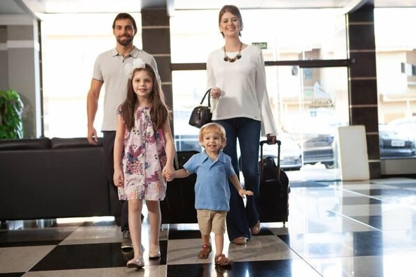 Una familia caminando por un vestíbulo con piso de tablones y un amplio ventanal al fondo.