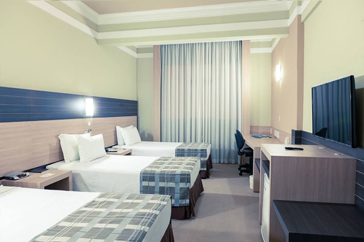 Habitación de hotel con dos camas, un escritorio, una silla, un televisor y un ventanal con cortinas.