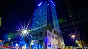 Un hotel de varios pisos con señalización iluminada, una entrada destacada y vista a la calle con coches aparcados y farolas.