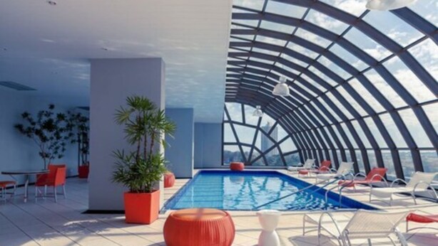 Un área de piscina interior moderna con techo curvo, sillones de descanso y plantas en macetas.