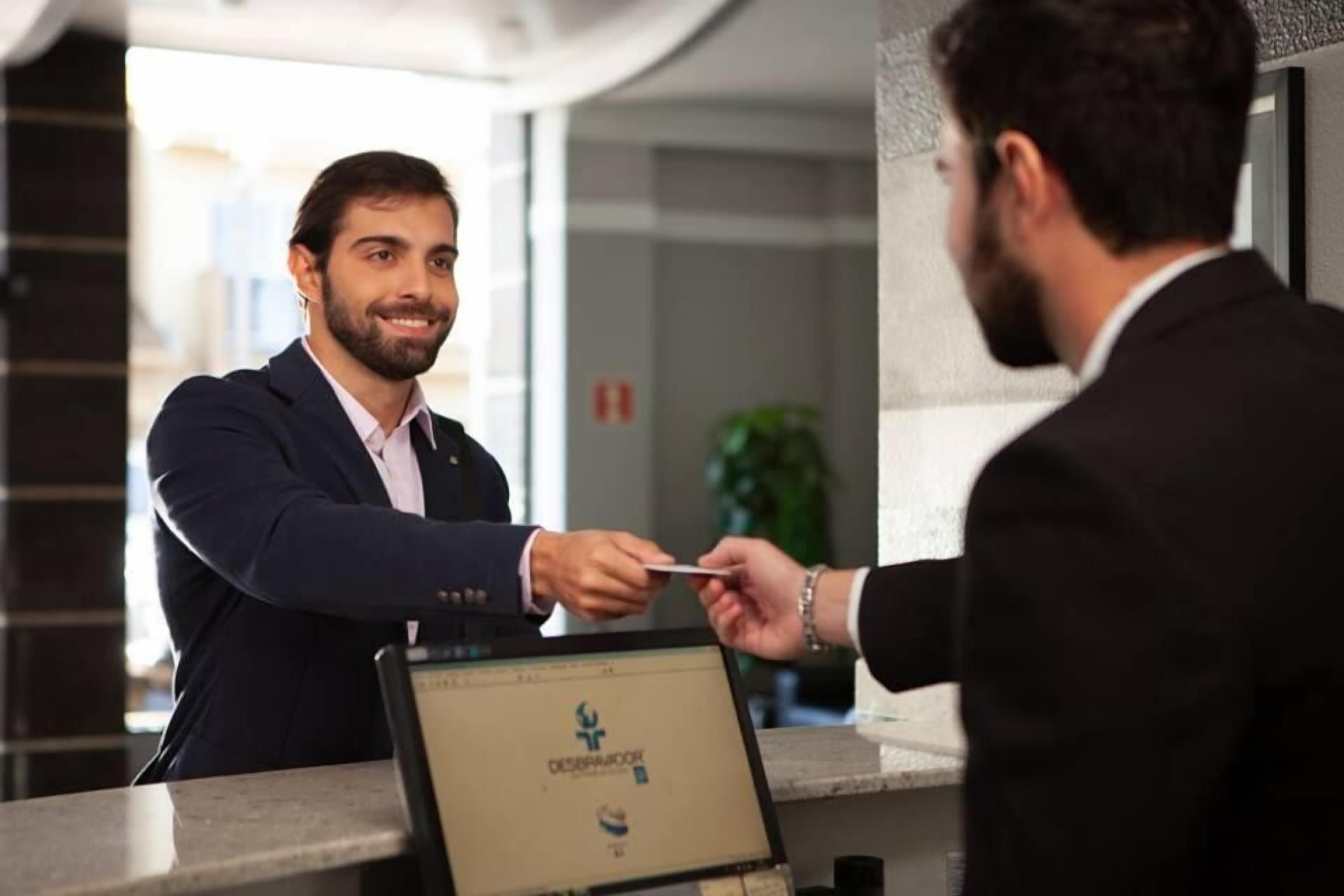 Uma mesa de recepção com um computador exibindo um logotipo e texto, indicando um ambiente de hotel ou empresarial.