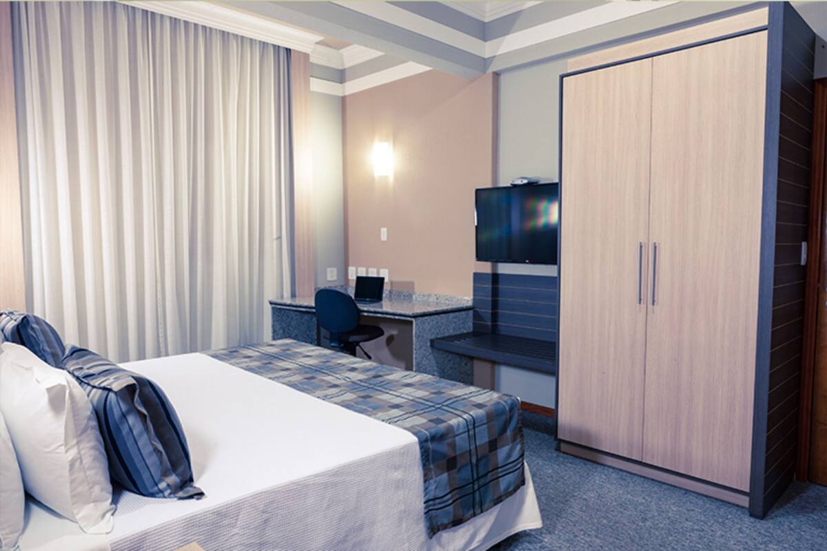 Una habitación de hotel con una cama, un escritorio, una computadora y un armario.