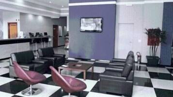 Un hall con suelo a cuadros, zonas de estar, un mostrador de recepción y un televisor montado.