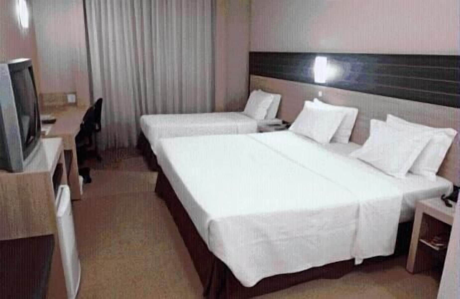 A hotel room with two single beds, a desk, and a television.