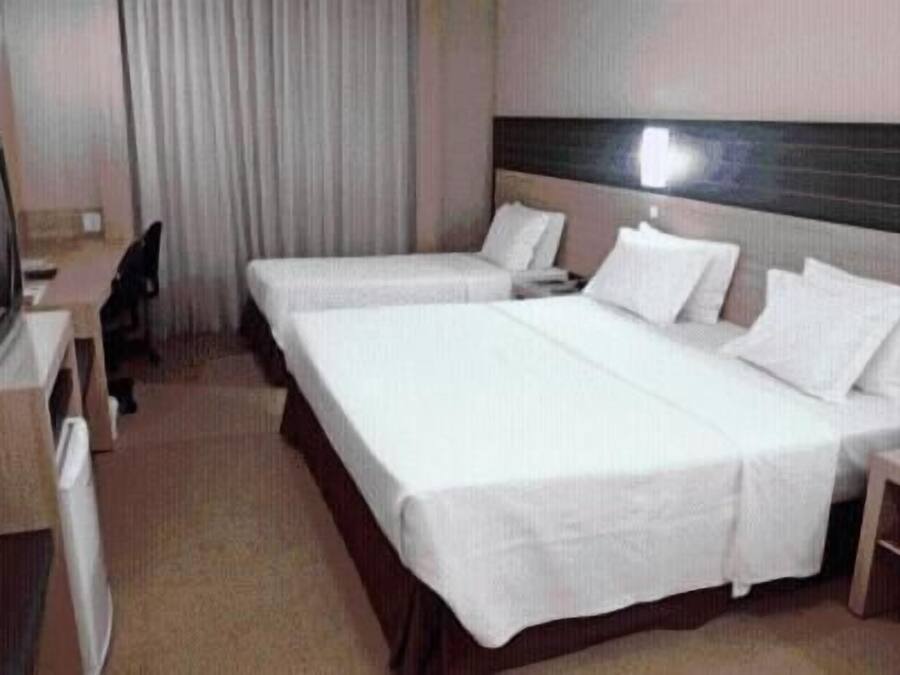 A hotel room with two single beds, a desk, and a television.