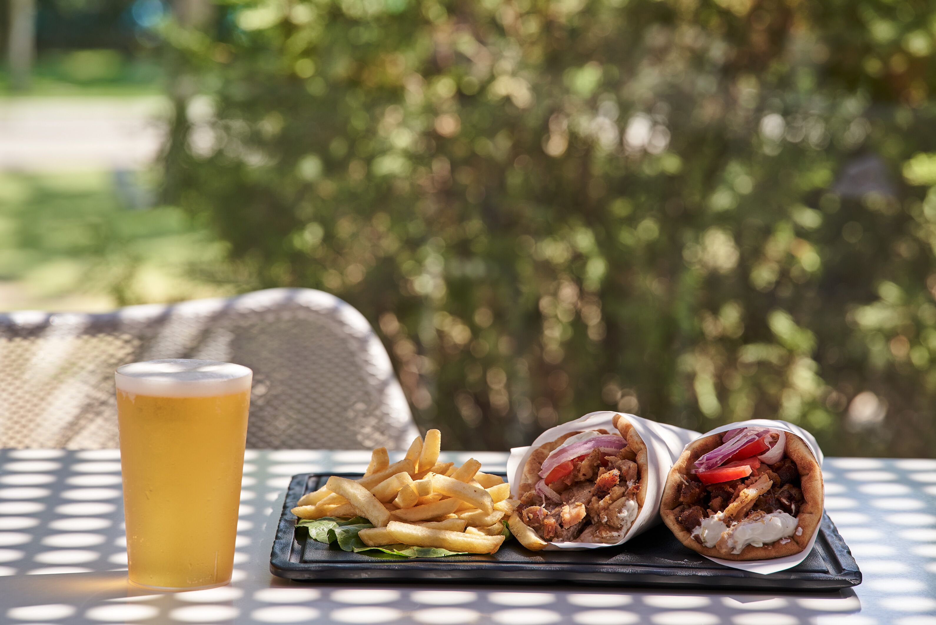 Un repas composé d’un verre de bière, d’une assiette de frites et d’un wrap garni de viande et de légumes, servi sur une table en plein air.