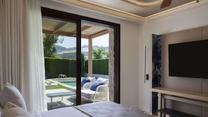 A bedroom with a large bed, a TV mounted on the wall, and a sliding glass door leading to a patio with outdoor furniture and a pool. - Atlantica Holiday Village Rhodes (Rhodes)