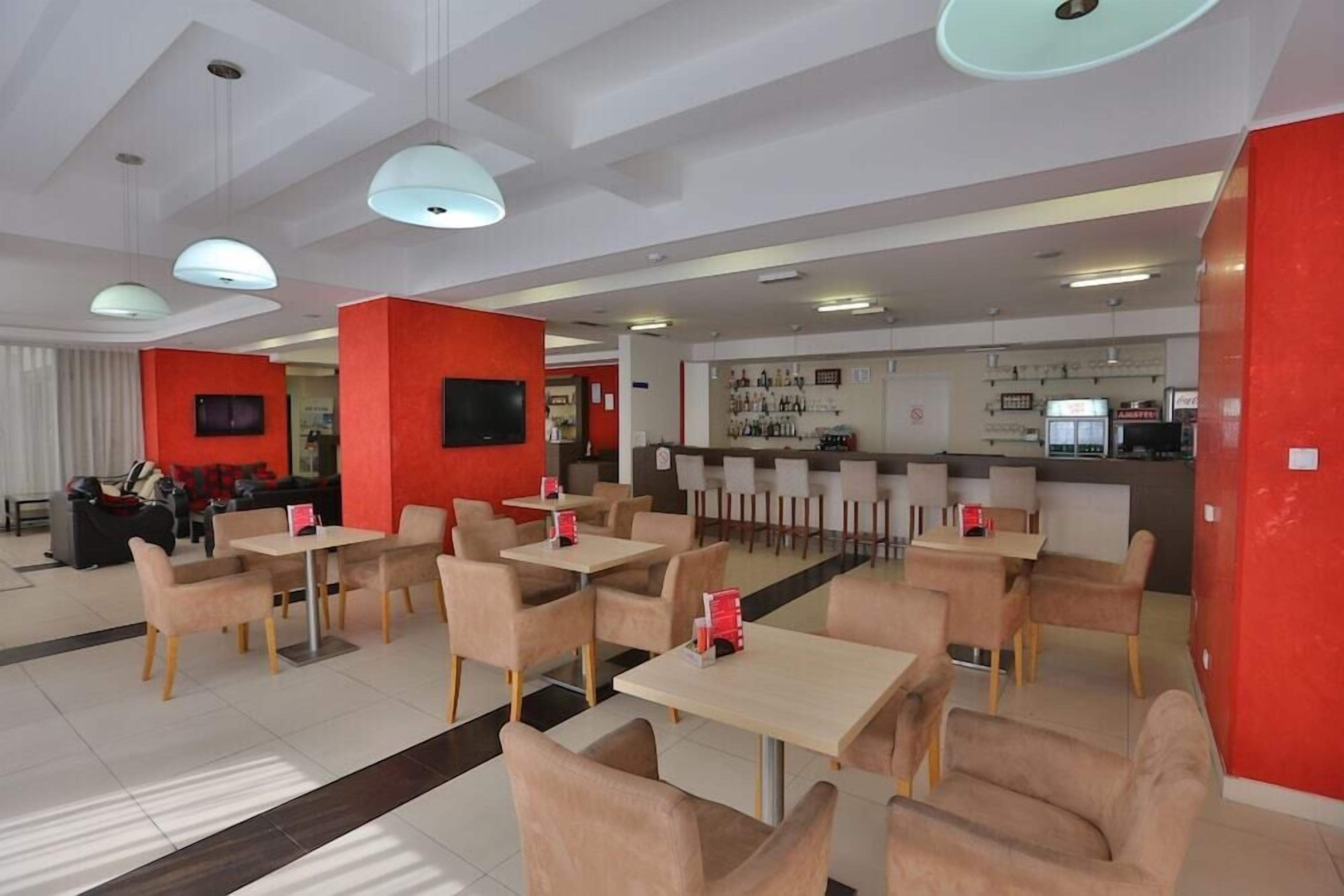 Un restaurante moderno con varias zonas de estar, incluyendo mesas y sillas, y una zona de bar con mostrador y estantes llenos de botellas.