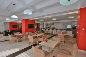 En moderne restaurant med flere siddeområder, blandt andet borde med stole, samt en bar med disk og hylder med flasker.