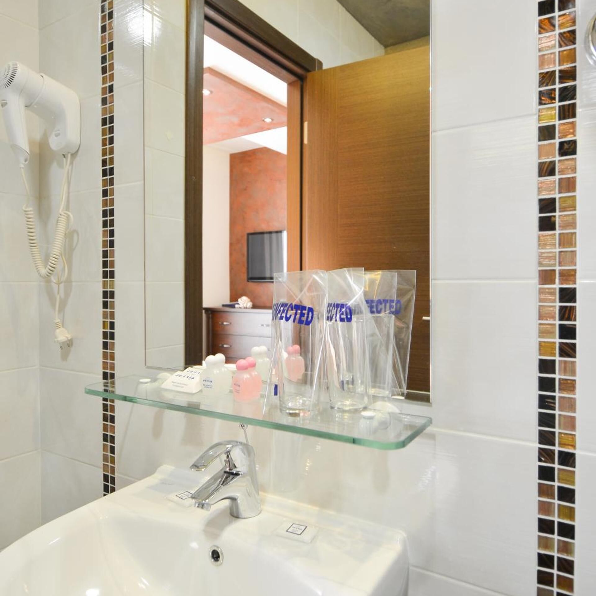 Un baño con un estante de vidrio que sostiene artículos de aseo, un lavabo blanco y un secador de pelo montado en la pared.